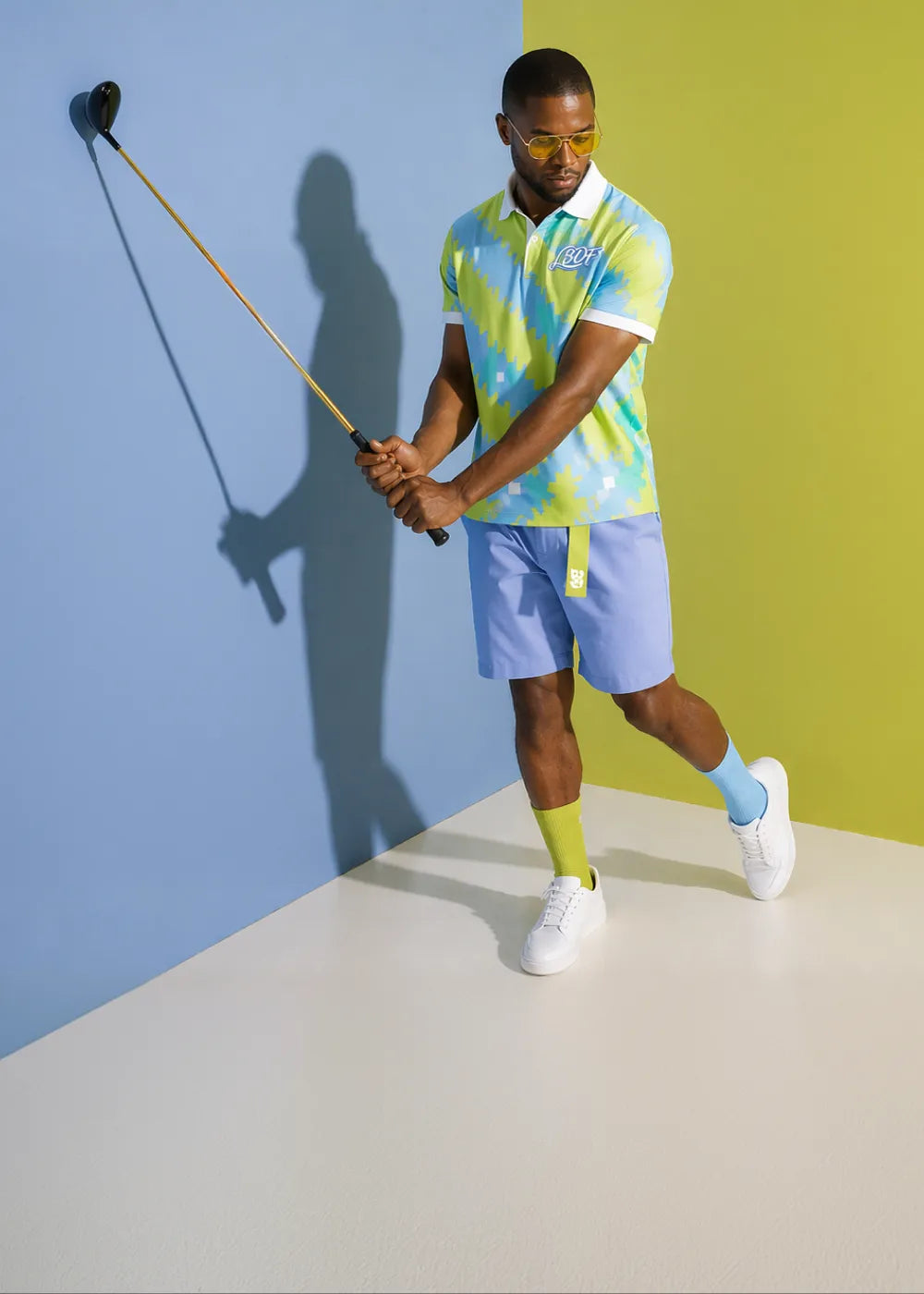 Man in colorful outfit holding a golf club against a multicolored background