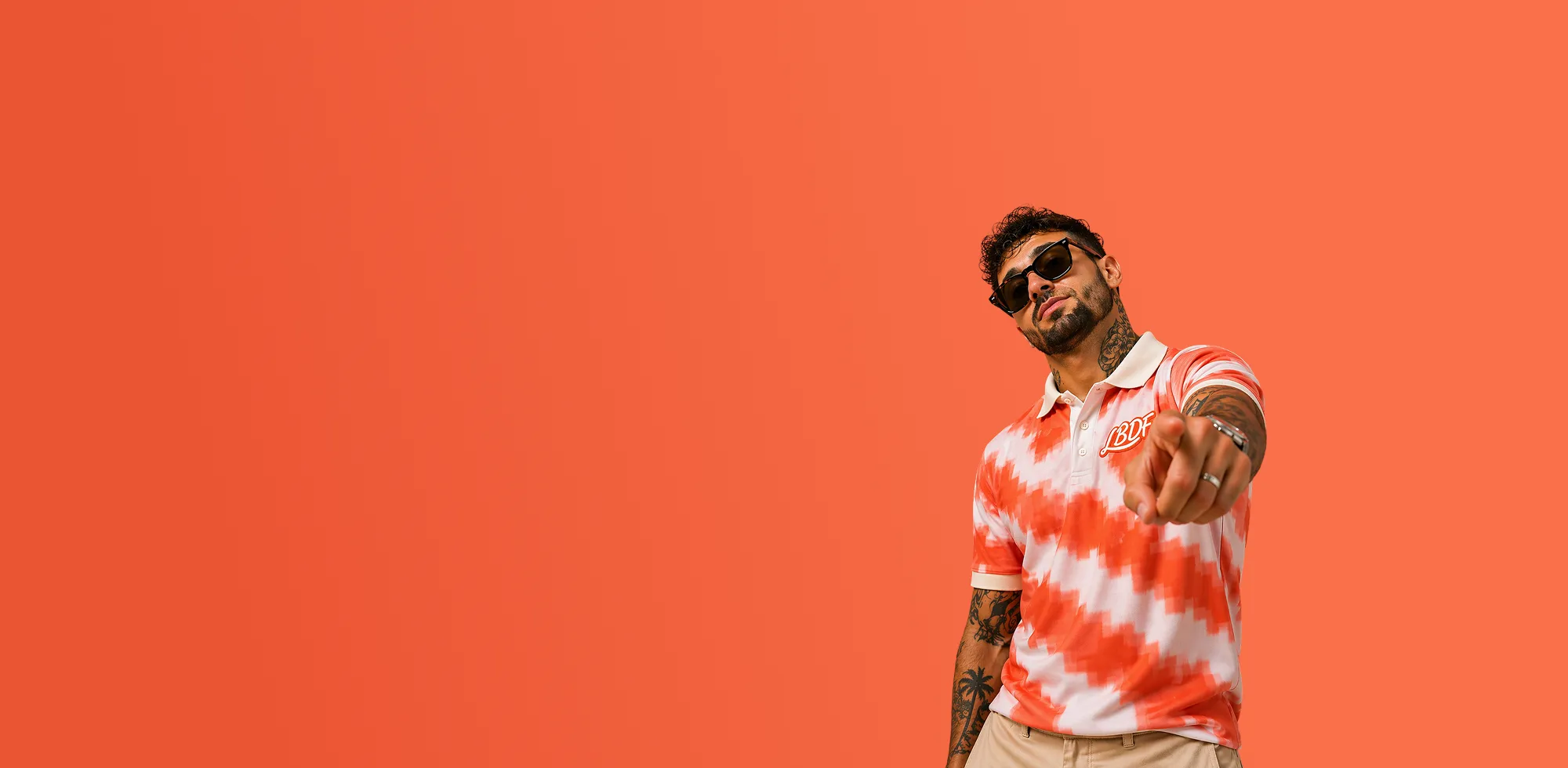 Man in a red and white striped shirt pointing towards the camera on an orange background